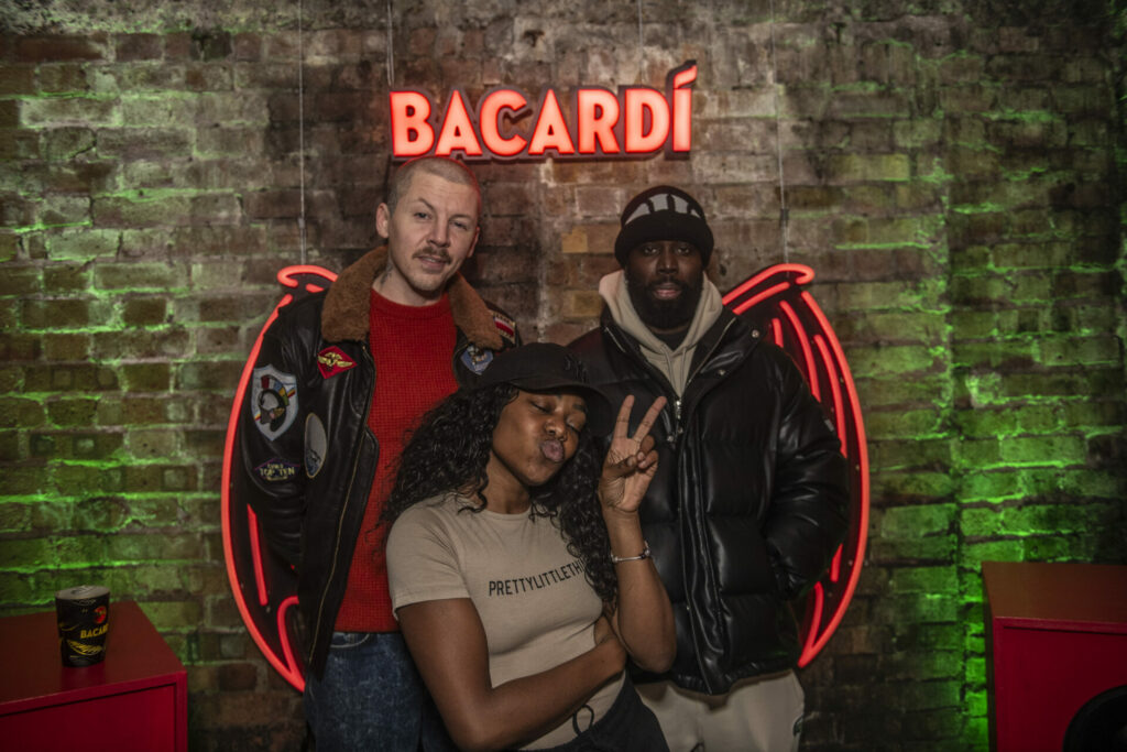 Three people stand in front of  BACARDÍ bat wings 