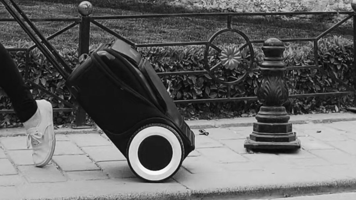 Black and white image of a piece of luggage being pulled on a street